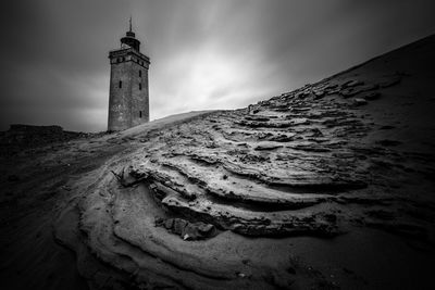 Lighthouse on beach by sea against sky