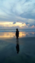 Rear view of silhouette man on beach against sky during sunset