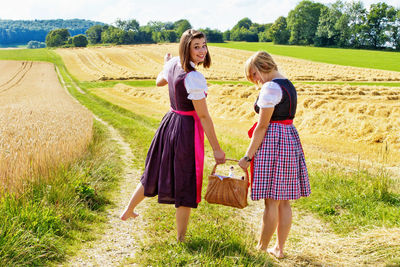 Portrait of young woman with friend holding basket on field