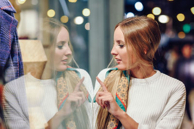 Young woman looking through store window in city at night