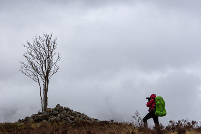 Female hiker photographing on field against cloudy sky