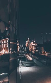 Illuminated street amidst buildings against sky at night