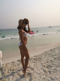 Side view of bikini woman standing on beach against clear sky