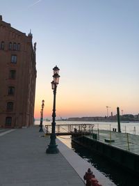 Street by buildings against sky during sunset