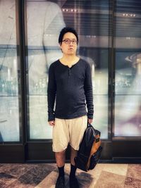 Portrait of young asian man in eyeglasses standing in front of illuminated reflective panels.