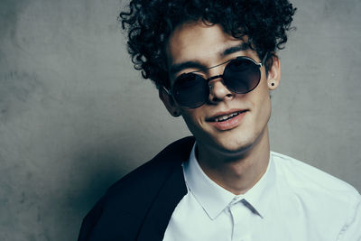 Portrait of young man wearing sunglasses standing against wall