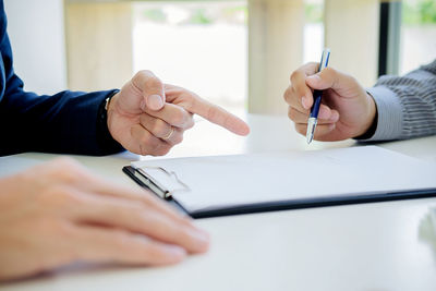 Midsection of businessman pointing while client signing contract on table