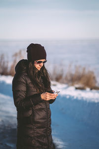 Woman wearing winter jacket using mobile phone on snow covered field