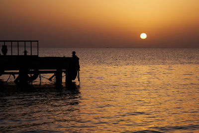 Silhouette pier over sea against sky during sunset