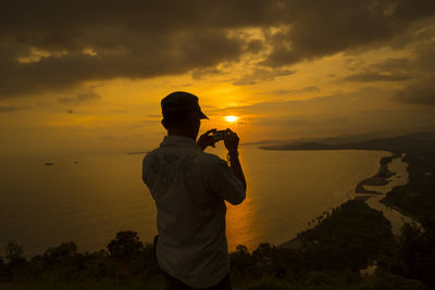 Rear view of man photographing at sunset