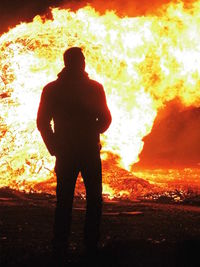 Rear view of silhouette man standing by fire at night