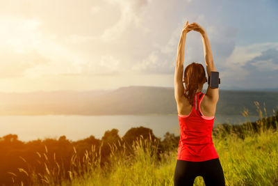 Rear view of young woman exercising on mountain against cloudy sky during sunset