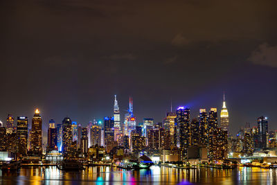 Illuminated buildings by river against sky at night