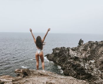 Rear view of woman walking on rocks by sea against sky