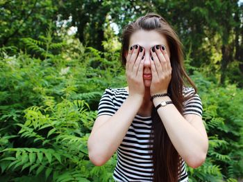 Young woman covering face while standing against plants