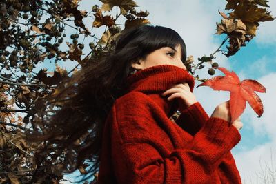 Portrait of young woman with autumn leaves against sky