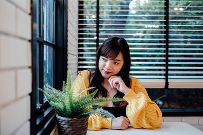 Portrait of young woman sitting on potted plant