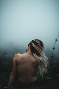 Rear view of shirtless young woman against sky