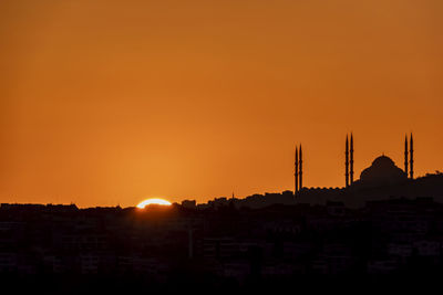 Silhouette buildings against orange sky during sunset