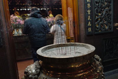 Incense sticks on container with people praying on background at temple