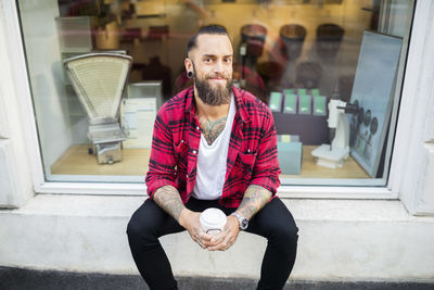 Portrait of happy owner with coffee sitting outside candy store