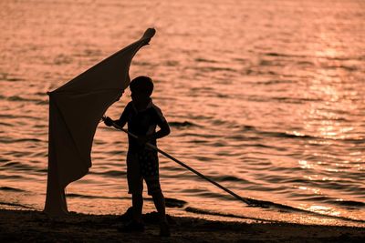Full length of boy holding parasol while standing at beach during sunset
