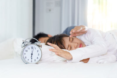 Man reaching alarm clock with woman on bed at home
