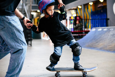 Close up of young skateboarder boy holding onto instructor's hands