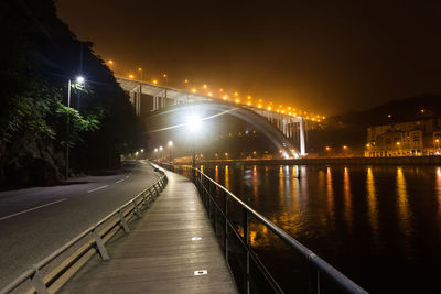 Illuminated bridge over river against sky at night