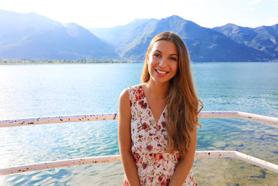 Portrait of smiling young woman standing against mountains and lake