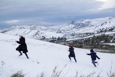 Side view of mother with children running on snow covered field at mountain