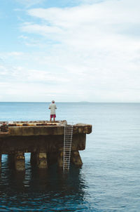 Rear view of man standing on abandoned pier in sea against sky
