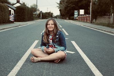 Portrait of a girl sitting along an empty road