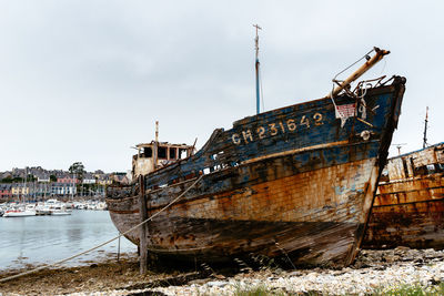 Abandoned boat moored at shore against sky