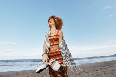 Side view of woman standing at beach against sky