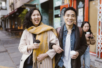 Portrait of male and female friends standing with arm in arm while holding disposable cups