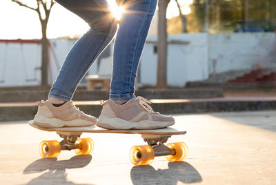 Impersonal closeup portrait of a wooden and pink skateboad cruiser with a girl in trainers on it