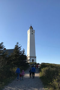 Rear view of people walking by lighthouse against clear blue sky