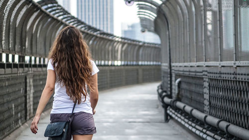 Rear view of woman walking on footbridge in city