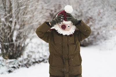 Cute little boy in funny winter hat walks during a snowfall. outdoors winter activities for kids.