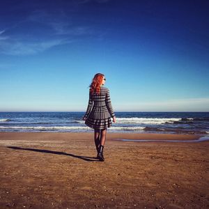 Rear view of woman standing on beach against sky