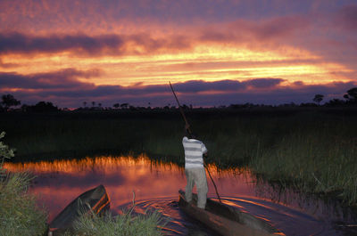 Rear view of man boating in lake against cloudy sky during sunset