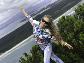 Portrait of young woman with arms outstretched standing against trees