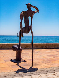 Cross sculpture on beach against clear blue sky