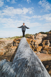 Woman balancing on log by rocks against sky