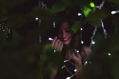 Close-up of smiling woman holding string light at night