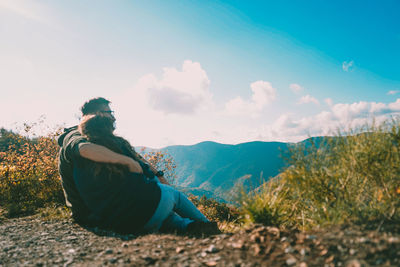 Rear view of couple sitting against mountain and sky