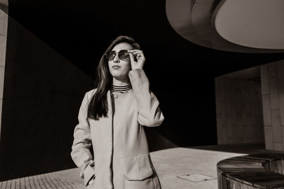 Fashionable woman wearing sunglasses while standing on footpath during sunny day