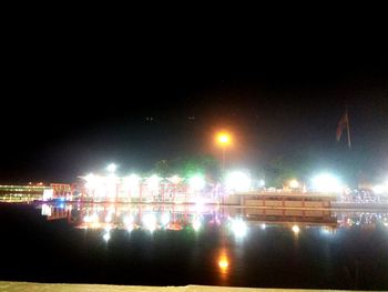 Illuminated city by river against sky at night