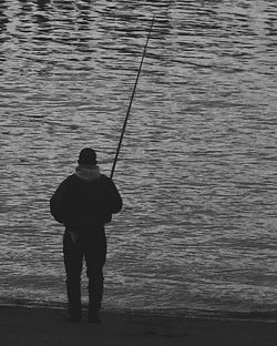 Rear view of silhouette man fishing at seashore